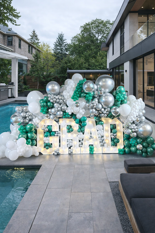 Graduation-themed balloon display with 'GRAD' letters by a poolside.