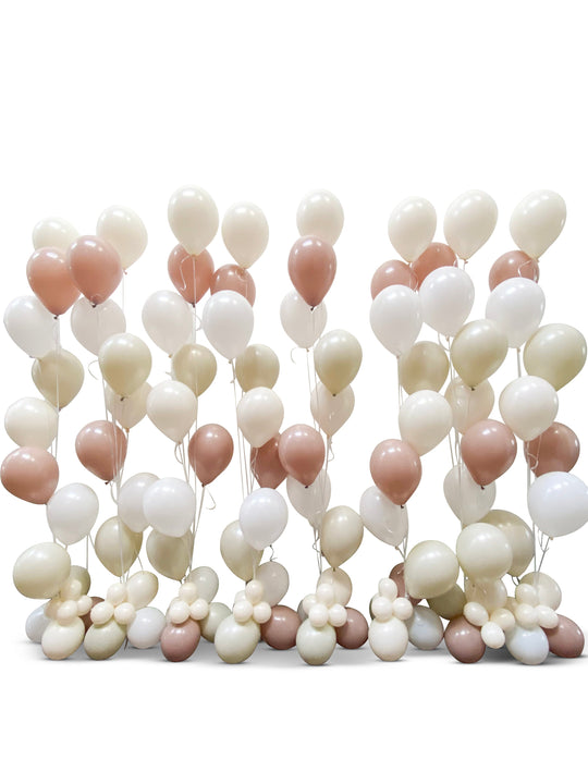 A wall of helium balloons in shades of white, rose gold, and silver, arranged to create a backdrop.